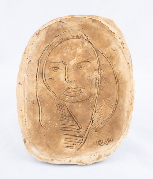 A shallow, dun-colored oval platter with an abstracted female face incised into, and ridged upon, the surface of the bowl.