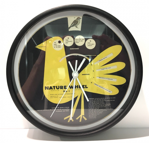 A round wall clock with the image of a yellow bird on a black background