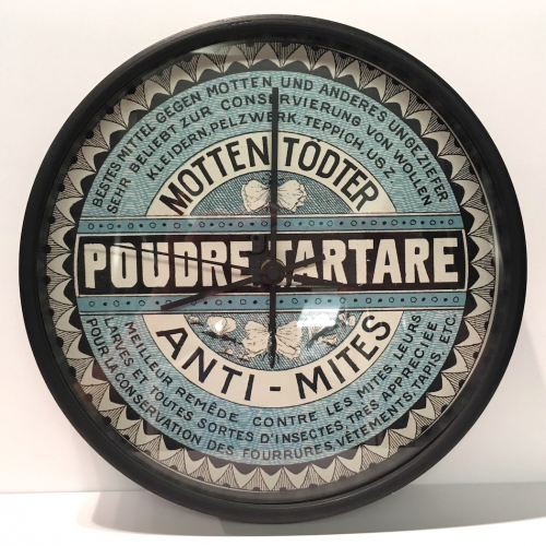 A round wall clock in blue, black, and white with a central banner stating "Poudre Tartare"