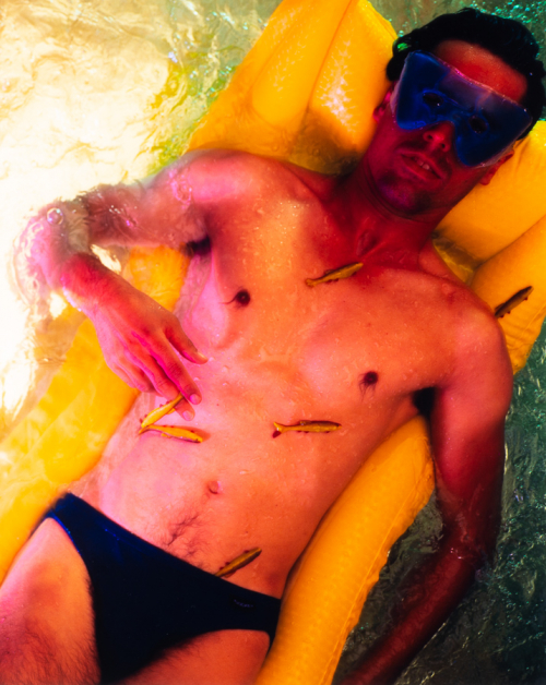 A male wearing a speedo in the water on a yellow float