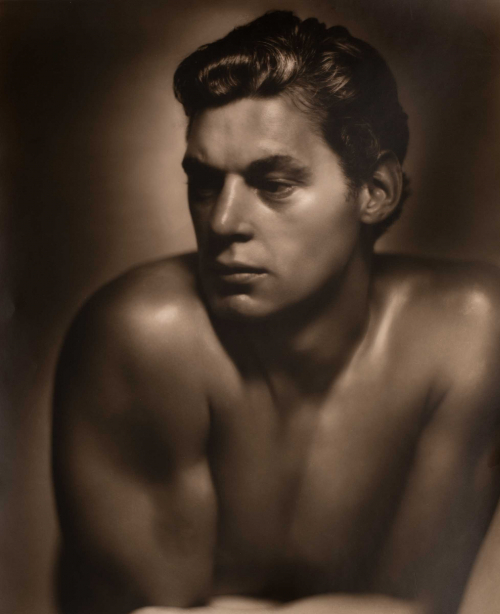 Bust of shirtless male leaning on crossed arms and looking to the left of the image
