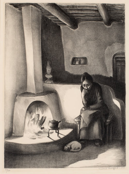 Black and white; old woman sitting in a chair next to fire with a cat next to her feet; in an adobe interior room