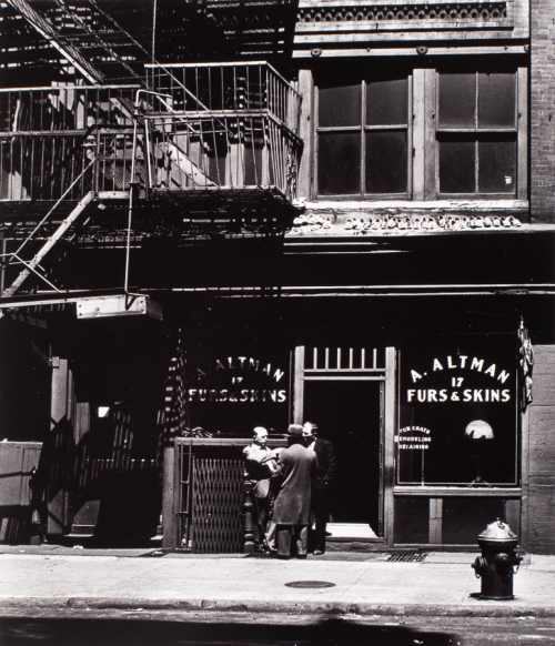 View of store-front with fire escape with 'Altman Furs and Skins 17' painted on both windows. Three men standing in front