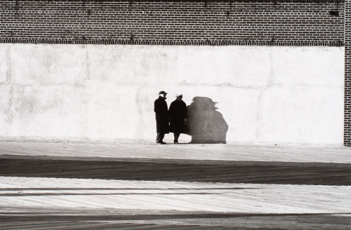 Brick building with large concrete section, man and woman dressed in winter clothing casting odd shadow on wall 
