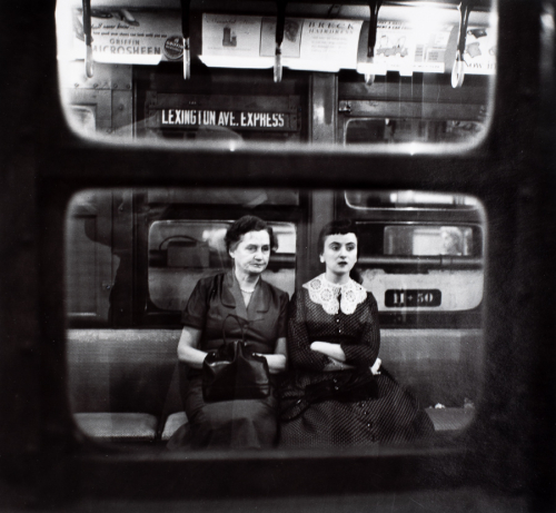 View of two women seated on subway seat seen through the subway window. Older woman on left and younger woman on right