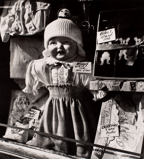 Standing doll nearly fills image. Surrounded by other dolls and little girls' merchandise.