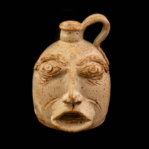 tiny face mug with a beige glaze, a right side handle, and prominent eyes, nose, and elliptical lips