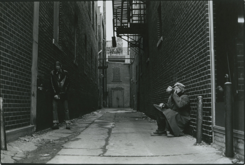 Two people in an alley, surrounded by brick buildings