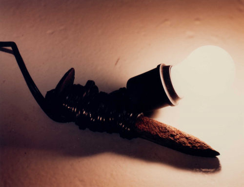 An image of a glowing light with its cable wrapped tightly around a rusty nail.