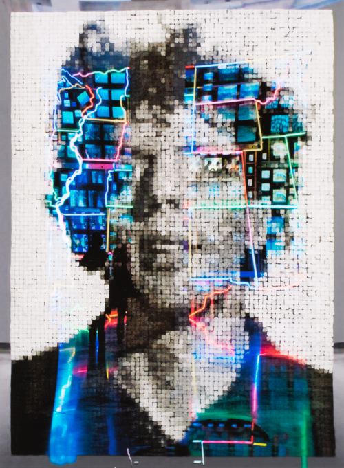 A black and white image of a male bust made with a series of small squares in a tight grid superimposed with neon imagery