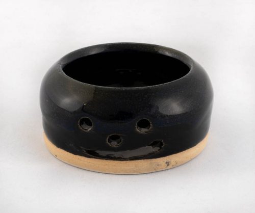A tiny black bowl-shaped vessel with a carved face.