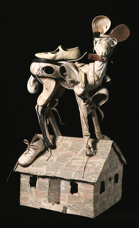 Leather and vinyl shoes, gloves, belts and electrical wire used to form a dog-shaped animal, standing on a house-shaped base