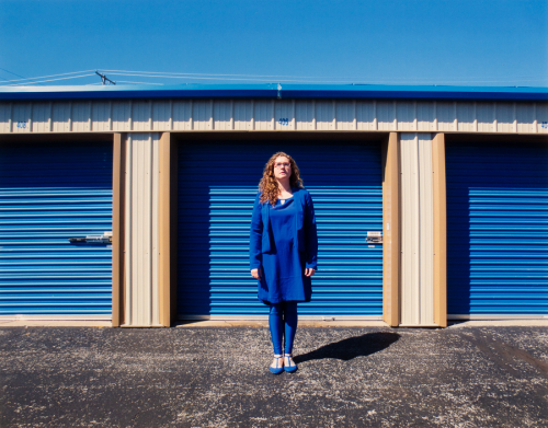 An image of a female dressed in blue standing in front of three blue storage unit doors
