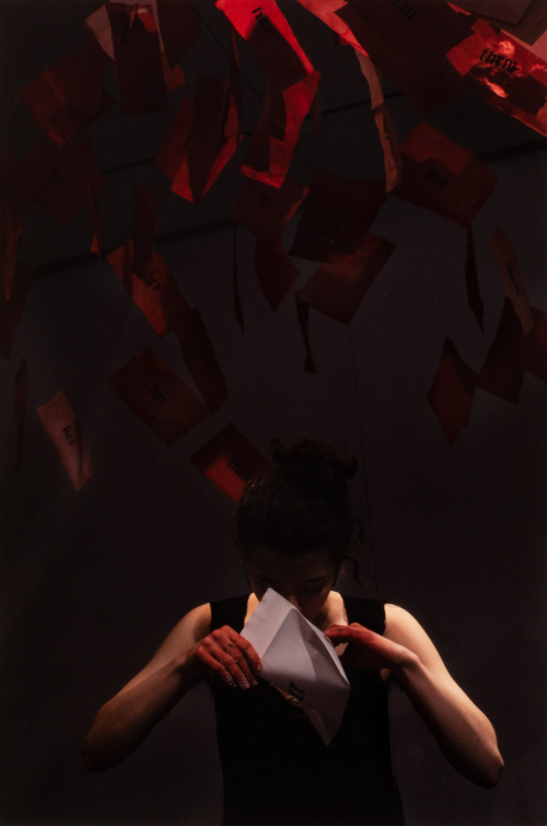 A female figure in black stands beneath numerous suspended red envelopes