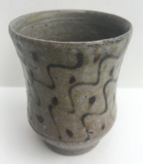 A small cup with wavy brown diagonal markings and dots on a beige glaze