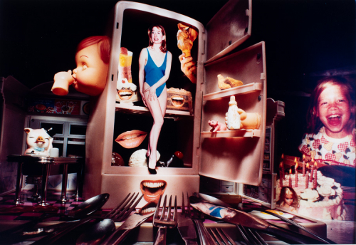 Extreme close-up of miniature refrigerator with open doors and images of mouths, food, and woman in bathing suit inside.