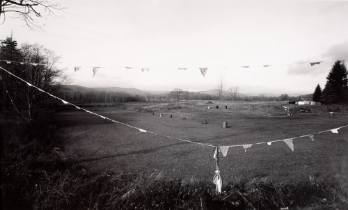 Landscape with open, grassy area in center of image. Barrels and sawhorses in center of area. Taller grass in foreground 