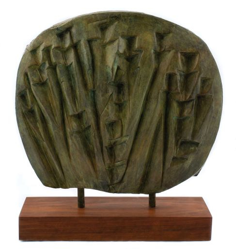 Circular, lens-shaped bronze with striated marks and a green patina. Mounted on a wooden base 