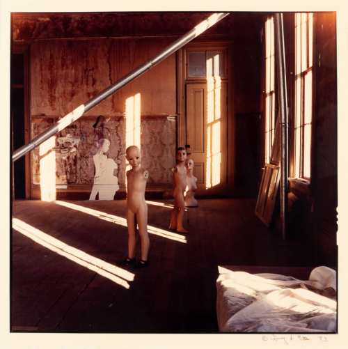 Old warehouse space with light streaming in through windows. Three mannequins throughout space, corner of white sheet in bottom