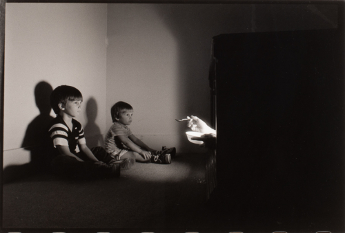 two little boys on floor in dark room with a TV on right with hands emerging from it holding a bowl and spoon 
