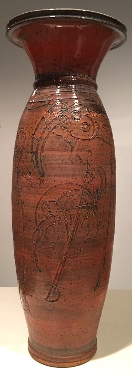 A tall cylindrical vase with a wide mouth glazed in orange glaze and abstract markings