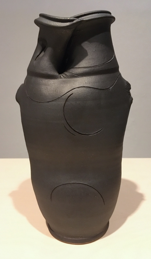 A small vase glazed in matte black with a cut and slightly collapsed rim
