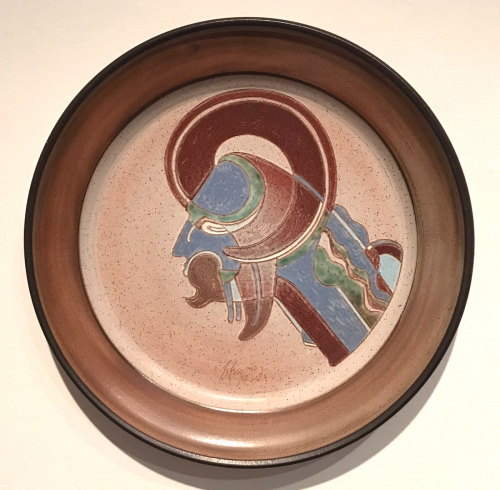 A large platter rimmed in brown glaze with a stylized image of a human bust in profile wearing curved horns