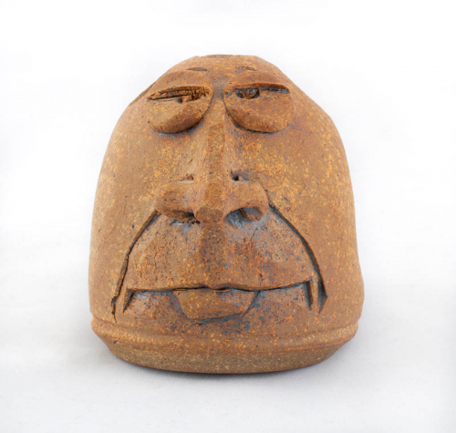 small face jug in the form of a toothbrush holder with a brown interior and two exposed front teeth protruding from closed lips.