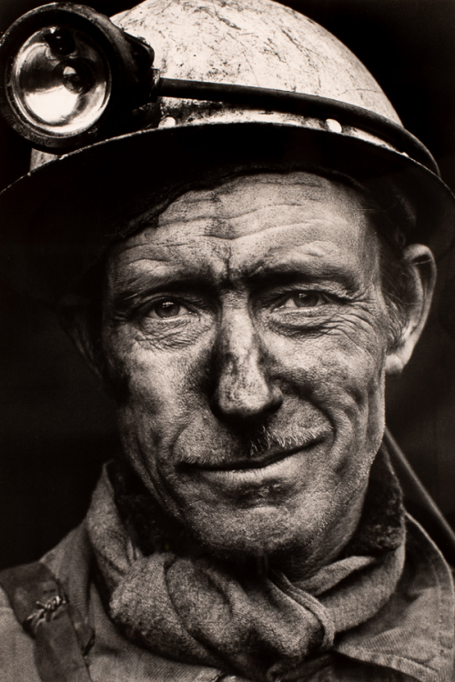 An image of a man's face smudged with coal wearing a miner's helmet