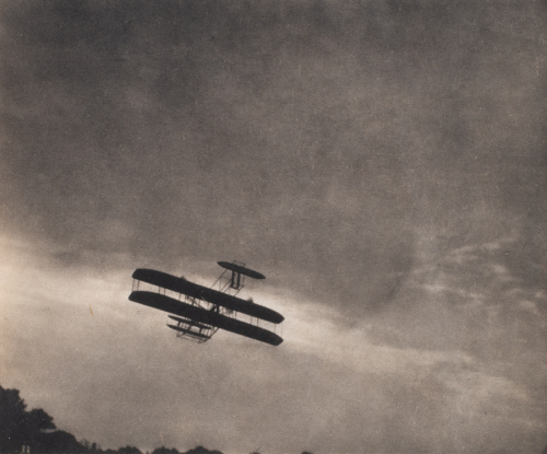 black and white image of an old airplane in flight; dark clouds