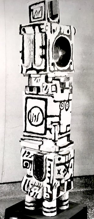 Tall, black and white totem pole-like sculpture with many symbols and markings.