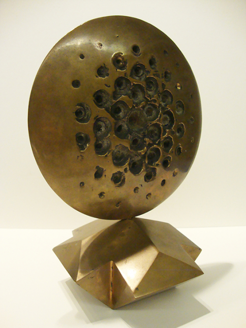 A shiny disc with numerous indentatinos on a geometric base