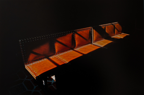 A photograph of an orange bench coming out of a shadowy background into a warm patch of light.