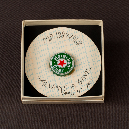 A 3-dimensional disc-shaped object with a Heineken Beer bottle cap pasted to gridded paper with hand-written words